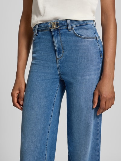 Vrouwenmodel draagt Flared Fit Jeans uit katoenmix van Liu Jo White in lichtblauw met logodetail en 5-pocketmodel, knoop- en ritssluiting, detailopname bovenlichaam. Context: dames jeans van Liu Jo White, elastische katoenmix, flared fit, logodetail, 5-pocketmodel, knoop- en ritssluiting, bandwijdte maat 27: 36 cm, binnenbeenlengte maat 27: 83 cm.
