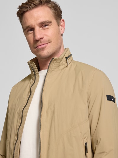 Männermodel trägt Regular Fit Jacke mit Opstaande kraag von bugatti in beige met logodetail en steekzakken, Nahaufnahme Oberkörper. Heren jack, tweewegritssluiting, elastische mouwboord, capuchon, maatinfo volgens context.