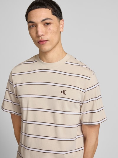 Männermodel trägt T-Shirt mit Logo-Stitching von Calvin Klein Jeans in Beige mit braunen Streifen, Reine Baumwolle, Gerader-Schnitt, Rundhalsausschnitt, Rückenlänge bei Größe M 69 cm, Nahaufnahme Oberkörper