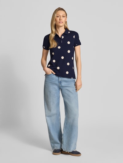Modelka kobieca nosi 'Poloshirt mit kurzer Knopfleiste' od Christian Berg Woman, bawełna z elastanem, krój slim fit, kolor granatowy z białymi groszkami, kołnierzyk polo, długość tyłu w rozm. S 61 cm, widok całej sylwetki z przodu.