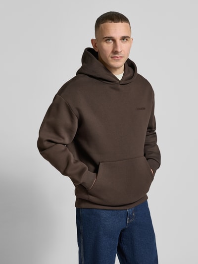 Männermodel trägt Hoodie mit Känguru-Tasche von REVIEW in Dunkelbraun, lockere Passform, Baumwollmischung, Nahaufnahme Oberkörper.