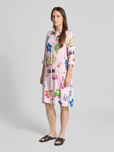 Frauenmodel trägt Relaxed Fit Hemdblusenkleid aus reiner Viskose von Milano Italy, pink mit buntem Comic-Print, Hemdblusenkragen und Knopfleiste, 3/4-Arm, Ganzkörperansicht von vorne.