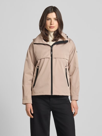 Kobiece modelka nosi kurtkę Jacke mit Stehkragen von khujo o kroju regular fit, stójka, zamek błyskawiczny, kieszenie zapinane na zamek błyskawiczny, długość tyłu w rozmiarze S: 60 cm, szerokość ramion w rozmiarze S: 51 cm, szerokość klatki piersiowej w rozmiarze S: 50 cm, długość rękawów w rozmiarze S: 54 cm, jasny beż z czarnymi detalami, matowa tekstura, widok całej sylwetki od przodu.