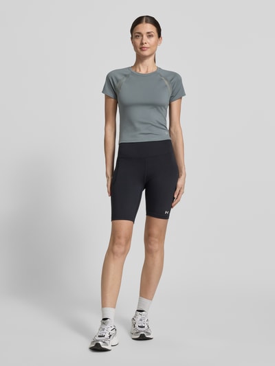Frauenmodel trägt T-Shirt mit Mesh-Einsätzen und Logo von Under Armour, Material-Mix mit Stretch-Anteil, Cropped, Rundhalsausschnitt, Logo, schwarzen Mesh-Einsätzen, Rückenlänge bei Größe S: 45 cm, schlichte Farben, glatte und luftige Textur, Ganzkörperansicht von vorne.