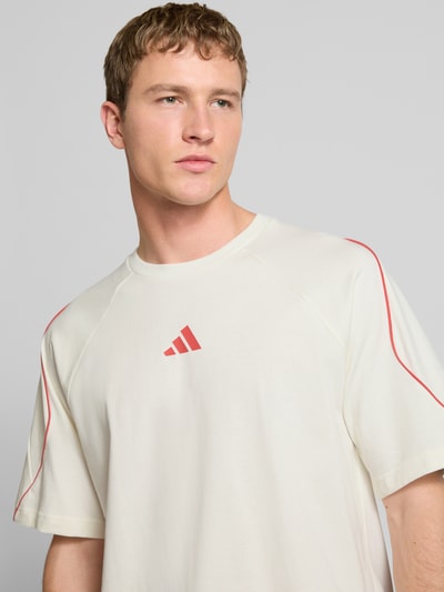 Männermodel trägt T-Shirt mit Label-Print von adidas Sportswear aus reiner Baumwolle, locker geschnitten, Nahaufnahme Oberkörper.