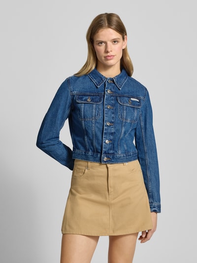 Kobiece model prezentuje Kurtka jeansowa o krótkim kroju z detalem z logo od Calvin Klein Jeans, bawełna, wykładany kołnierz, kieszenie na piersi, listwa guzikowa, kolor niebieski, długość tyłu 44 cm, szerokość ramion 40 cm, szerokość klatki piersiowej 44 cm, długość rękawów 61 cm, widok całej sylwetki z przodu.