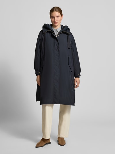 Vrouwenmodel draagt rechte lange jas met capuchon, zij-klepzakken, ritssluiting en drukknoop, binnenvoering uitneembaar, Model 'AKIRA' van g-lab, donkerblauw, Ganzkörperansicht von vorne. Ruglengte maat S: 106 cm, schouderbreedte: 58 cm, borstwijdte: 69 cm, mouwlengte: 59 cm.