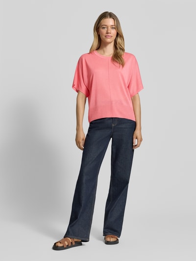Frauenmodel trägt Strickshirt aus Viskose-Mix mit Teilungsnaht von More & More in Rosa, kombiniert mit Jeans; Ganzkörperansicht von vorne. Damen Regular Fit, Rundhalsausschnitt, Rückenlänge 60 cm, Ärmellänge 35 cm.