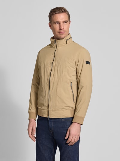 Mannelijk model draagt Regular Fit Jack met opstaande kraag van bugatti in beige, met tweewegritssluiting, logodetail, steekzakken. Ganzkörperansicht von voren.
