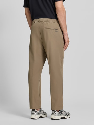 Männermodel trägt Tapered Fit Anzughose aus bügelleichtem Material Modell 'T_CONVERT' von BOSS Green in Beige, Ganzkörperansicht Rückansicht, unifarbene Optik, Regular Fit, Cropped-Länge, Vier-Wege-Stretch, Tunnelzug, schnell trocknend, integriertes Kartenetui, seitliche Eingrifftaschen.