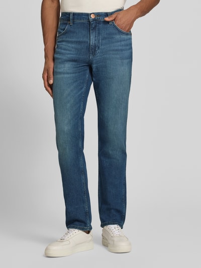 Männermodel trägt Straight Fit Jeans im 5-Pocket-Design Modell 'Greensboro' von Wrangler, Baumwoll-Mix, Gerader-Schnitt, Knopf-Reißverschluss, mittleres Blau, glatte Textur, Ganzkörperansicht von vorne.
