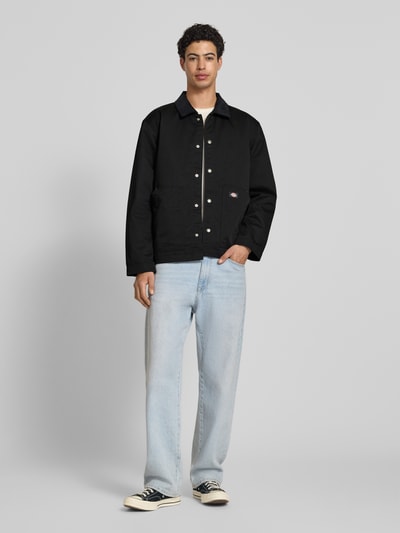 Männermodel trägt Jacke mit Umlegekragen und Label-Detail von Dickies, schwarz, Material-Mix, Regular-Fit, Eingrifftaschen, Ganzkörperansicht von vorne, Rückenlänge 75 cm, Schulterbreite 47 cm, Brustweite 64 cm, Ärmellänge 66 cm.