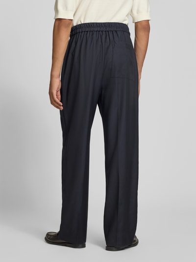 Männermodel trägt Stoffhose aus Woll-Mix von Officine Générale in Dunkelblau, elastischer Bund, Bundfalten, Ganzkörperansicht Rückansicht.