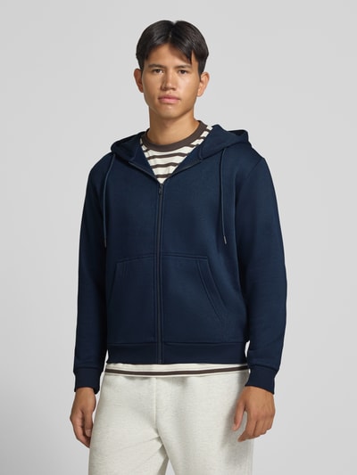Männermodel trägt Regular Fit Sweatjacke aus Baumwoll-Mix Modell 'BRADLEY' von JACK & JONES in Dunkelblau, Vorderansicht, Ganzkörperansicht von vorne. Rückenlänge 67 cm, Ärmellänge 68 cm, Kapuze mit Tunnelzug, Känguru-Tasche, elastische Abschlüsse.