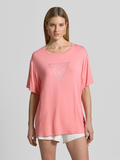 Modelka kobieca ma na sobie damski t-shirt z mieszanki wiskozy o luźnym kroju, okrągły dekolt, nadruk z logo, tunel, model 'COULISSE' od Guess, długość tyłu w rozmiarze S: 70 cm, widok całej sylwetki z przodu.