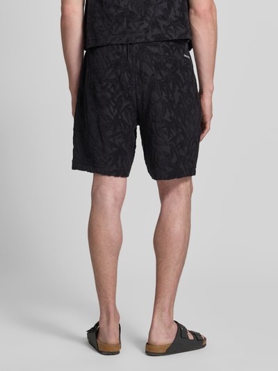 Männermodel trägt Regular Fit Sweatshorts aus reiner Baumwolle von Marc O'Polo mit floralem Allover-Muster, Jersey-Frottee, Ganzkörperansicht Rückansicht.