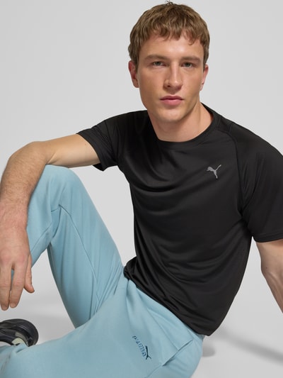 Männermodel trägt T-Shirt mit Label-Print von PUMA PERFORMANCE in Schwarz, Material-Mix mit Stretch-Anteil, Regular-Fit, Nahaufnahme Oberkörper.