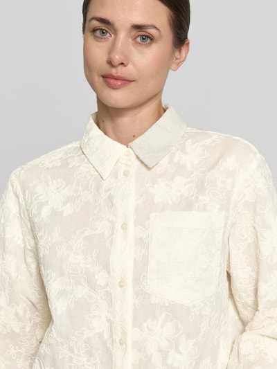 Vrouwenmodel draagt Bluse mit Brusttaschen Modell 'Sylvia' van MSCH Copenhagen in gebroken wit, rechte fit, katoenen stof met borduurdetails, borstzak, hemdkraag, knoopsluiting, detailopname bovenlichaam.