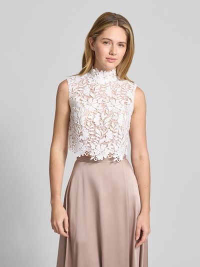 Frauenmodel trägt Regular Fit Top in semitransparentem Design von Luxuar mit Allover-Spitzen-Optik, Stehkragen, Ärmelloses-Design, integrierte Pads, Farbe weiß, Vorderansicht, Nahaufnahme Oberkörper.