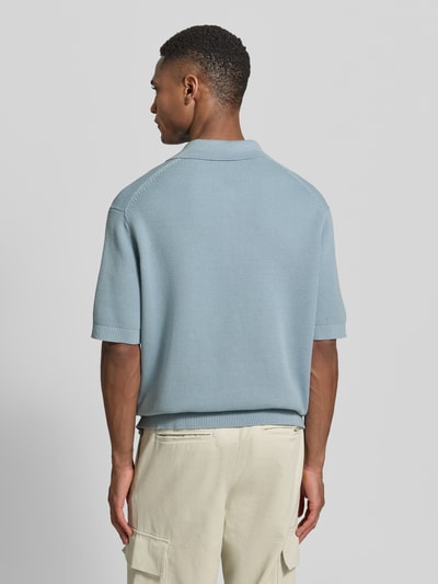 Männermodel trägt Relaxed Fit Poloshirt aus reiner Baumwolle Modell 'DANE' von SELECTED HOMME in Hellblau mit Strickoptik, Ganzkörperansicht Rückansicht.