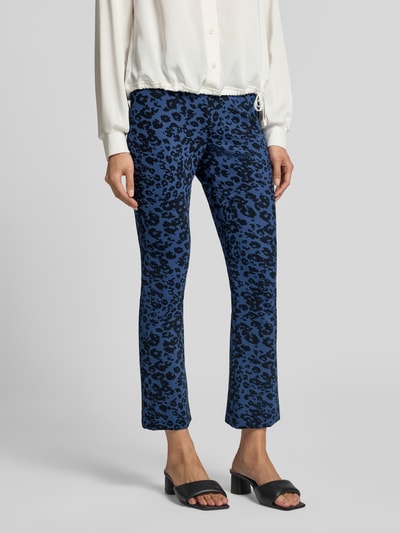 Frauenmodel trägt Flared Fit Leggings mit Allover-Animal-Print von Marc Cain in Blau mit elastischem Bund und Logo-Detail, Nahaufnahme Unterkörper.