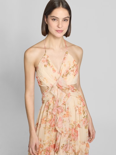 Frauenmodel trägt Regular Fit Midikleid mit Rüschenbesatz von ADLYSH, floraler Allover-Print, Halterneck, V-Ausschnitt, Rückenausschnitt, Falten-Optik, sanfte Beige- und Rosatöne, weich fließender Stoff, Ganzkörperansicht von vorne.