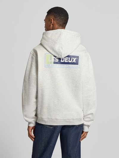 Männermodel trägt Hoodie mit Logo-Print Modell 'Chase' von Les Deux aus grauer Baumwolle, Loose Fit, Rückansicht, Ganzkörperansicht.