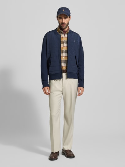 Männermodel trägt navyblaue Sweatjacke mit gerippten Abschlüssen von Polo Ralph Lauren, Regular-Fit, Stehkragen, Reißverschluss, Label-Stitching, Pattentaschen mit Druckknopfverschluss, Rückenlänge 57 cm, Ärmellänge 70 cm, Ganzkörperansicht von vorne.