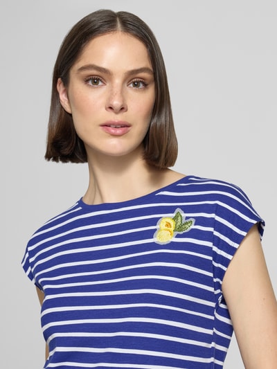 Kobiecy model nosi T-Shirt mit Motiv-Stitching und Rundhalsausschnitt od Marc Cain, bawełna z elastanem, krój regular fit, paski w kolorze niebieskim i białym, aplikacja z motywem cytryny, długość tyłu w rozmiarze 36: 52 cm, zbliżenie na górną część ciała.