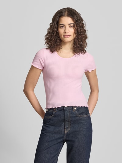 Modelka kobieca nosi Slim Fit T-Shirt mit Viskose-Anteil Modell 'EMMA' od Only, różowy, prążkowana struktura, krótki rękaw, frill, tkanina stretch jacquard, widok całej sylwetki z przodu.
