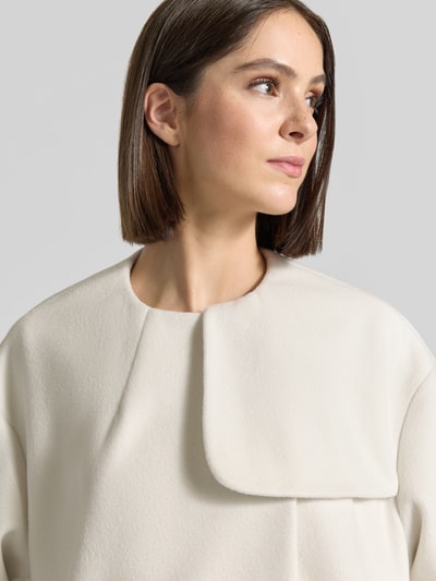 Frauenmodel trägt Mantel mit Rundhalsausschnitt und Bindegürtel von Armani Exchange in Creme, Material-Mix mit Viskose-Anteil, Nahaufnahme Oberkörper.