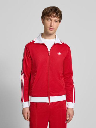 Männermodel trägt Regular Fit Sweatjacke mit Stehkragen Modell 'Classic' von adidas Originals in Rot mit weißen Details, Nahaufnahme Oberkörper. Baumwoll-Mix, Logo-Stitching, Zweiwege-Reißverschluss, Eingrifftaschen, elastische Abschlüsse.