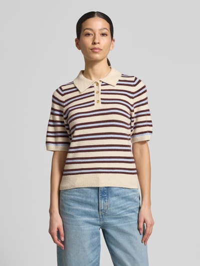 Modelka kobieca ma na sobie Regular Fit Strickpullover mit Woll-Anteil Modell 'CANNA' od Vero Moda, kolorowy, prążkowany, krój regular fit, kołnierzyk polo, dekolt w serek, krótki rękaw, zakończenia prążkowane, dzianina z domieszką wełny, widok całej sylwetki z przodu.