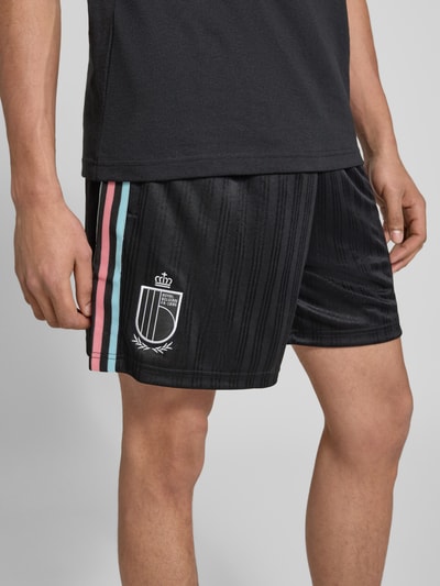 Männermodel trägt Regular Fit Sweatpants mit Label-Detail Modell 'Belgien 26' von adidas Originals, schwarze Unifarbe, Nahaufnahme Oberschenkel.