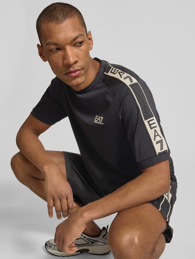 Męski model nosi T-shirt aus Viskose-Mix mit Logo von EA7 Emporio Armani, krój regular fit, okrągły dekolt, długość tyłu 70 cm, całkowity widok z przodu.