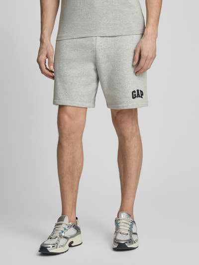 Männermodel trägt Sweatshorts mit elastischem Bund von GAP aus Baumwoll-Mix, Relaxed-Fit, Logo, hellgrau, Ganzkörperansicht von vorne.