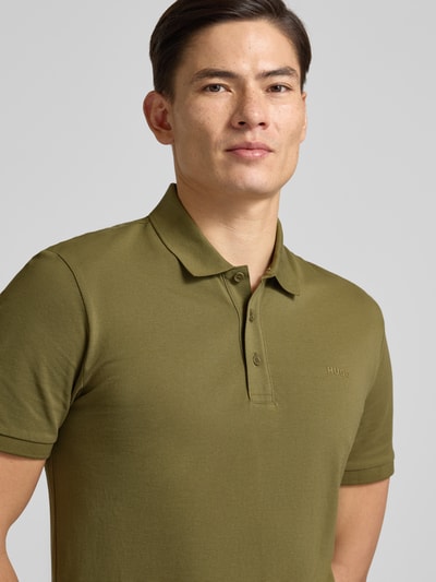 Männermodel trägt Regular Fit Poloshirt aus reiner Baumwolle Modell 'DONOS222' von HUGO, Optik: Unifarben, Label-Print, Nahaufnahme Oberkörper.