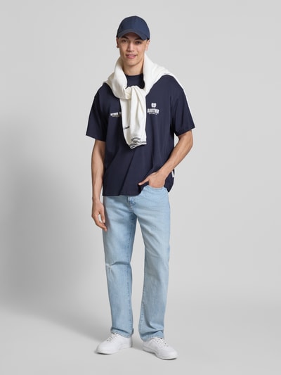 Männermodel trägt Regular Fit T-Shirt mit Logo-Print von ANOTHER COTTON LAB in Dunkelblau, reine Baumwolle, helle Jeans, Ganzkörperansicht von vorne.
