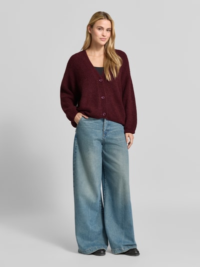Frauenmodel trägt Oversized Cardigan mit Alpaka-Anteil Modell 'East' von American Vintage in Strick-Optik, bordeaux, Ganzkörperansicht von vorne.