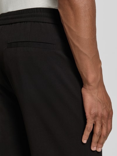 Männermodel trägt Relaxed Fit Sweatpants mit Viskose-Anteil von Lindbergh in Schwarz, Elastischer-Material-Mix, Detailaufnahme Rückansicht. Bundweite bei Größe M: 41 cm, Innenbeinlänge bei Größe M: 79 cm, Bügelfalten, elastischer Bund mit Tunnelzug.