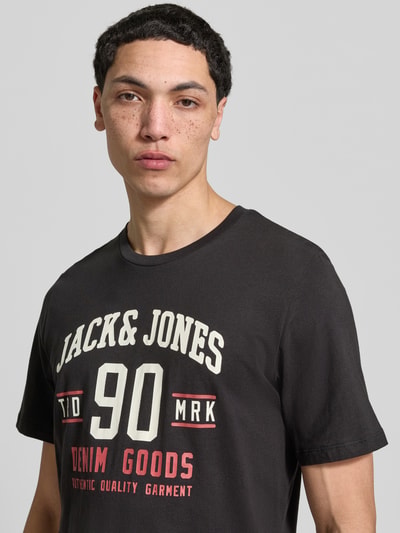 Mannenmodel draagt T-Shirt met Label-Print im 3er-Pack Modell 'ETHAN' van Jack & Jones van zuiver katoen, recht fit, ronde hals, zwart met witte en rode print, Nahaufnahme bovenlichaam.