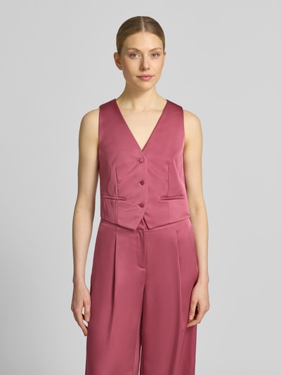 Frauenmodel trägt Weste aus Satin mit V-Ausschnitt von Jake*s Cocktail in Rosa, glatte Textur, Paspeltaschen, Slim Fit, Ganzkörperansicht von vorne.