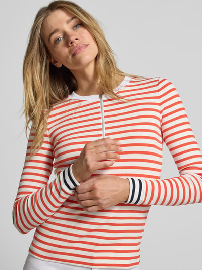 Frauenmodel trägt Longsleeve mit Rundhalsausschnitt und Reißverschluss von Marc Cain, Baumwoll-Elasthan-Mix, Regular Fit, rot-weiß gestreift, glatte Textur, Ganzkörperansicht von vorne.