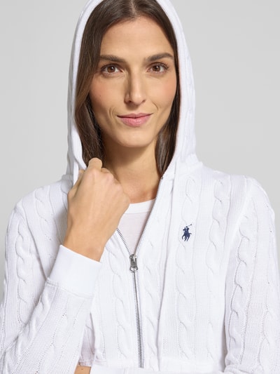 Kobieta modelka ma na sobie Regular Fit Kardigan rozpinany z kapturem z bawełny od Polo Ralph Lauren, wyhaftowane logo, wpuszczane kieszenie, prążkowane wykończenia, zamek błyskawiczny, kolor biały, faktura dzianiny, zbliżenie na górną część ciała.