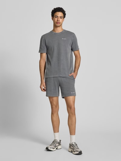Mężczyznę model nosi Shorts mit Strukturmuster und elastischem Bund von CHAMPION, bawełniany miks, krój regular fit, szare, fakturowana tkanina, label-stitching, szerokość w rozmiarze M 40 cm, długość wewnętrzna nogawki 19 cm, widok całej sylwetki z przodu.