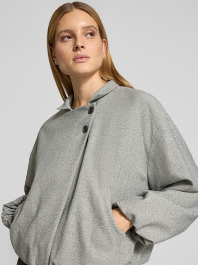 Vrouwenmodel draagt Boxy Fit Kurzblazer met Woll-Anteil Model 'JAVATA' van BOSS in gemêleerde look, reverskraag, twill, zij-steekzakken, dubbele knoopsluiting, elastische mouw- en rompzoom, applicaties. Nahaufnahme bovenlichaam.