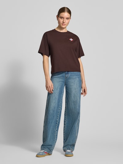 Vrouwenmodel draagt 'Oversized Fit T-Shirt aus reiner Baumwolle mit Logo-Stickerei' van closed, puur katoen, oversized fit, geborduurd logo, bloemenborduursel, halflange mouwen, verlaagde schouders, ruglengte bij maat S: 52 cm, bruine kleur, rechte vormen, zachte textuur, volledige lichaamsaanzicht van voren.