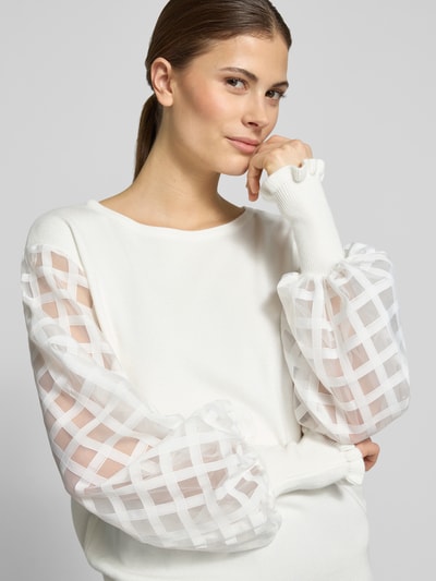 Frauenmodel trägt Strickpullover aus Viskose-Mix mit Rundhalsausschnitt von Apricot, semitransparente Ärmel, Nahaufnahme Oberkörper.