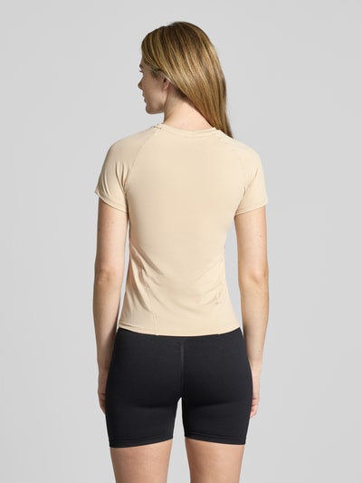 Modelka nosi T-Shirt mit Rundhalsausschnitt und Logo od aim'n, kolor beżowy, krój slim fit, materiał z domieszką stretchu, widok całej sylwetki z tyłu.