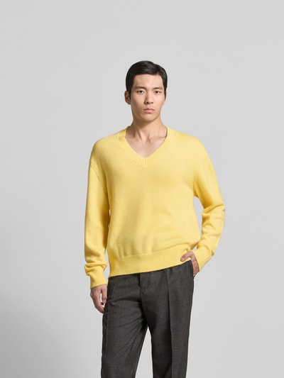 Männermodel trägt Kaschmirpullover in Strick-Optik von Officine Générale in Gelb, lockere Passform, V-Ausschnitt, Ganzkörperansicht von vorne.